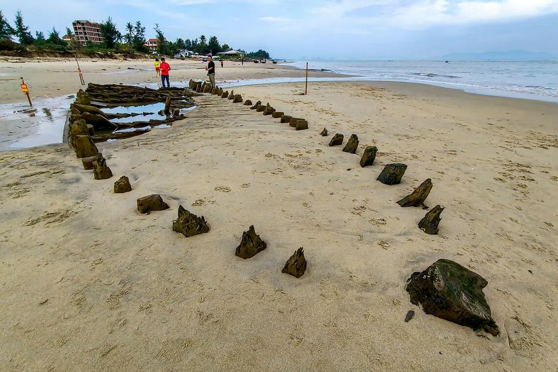 People stand next to a centuries-old shipwreck uncovered in the aftermath of Typhoon Kalmaegi on a beach off the Hoi An coast in central Vietnam, on November 10, 2025. Initially discovered in 2023, the at least 17.4-metre (57-foot) vessel -- whose heavy wood-ribbed hull survived hundreds of years of rough seas almost perfectly intact -- was resubmerged before authorities could reclaim it. (Photo by Tam Xuan / AFP)