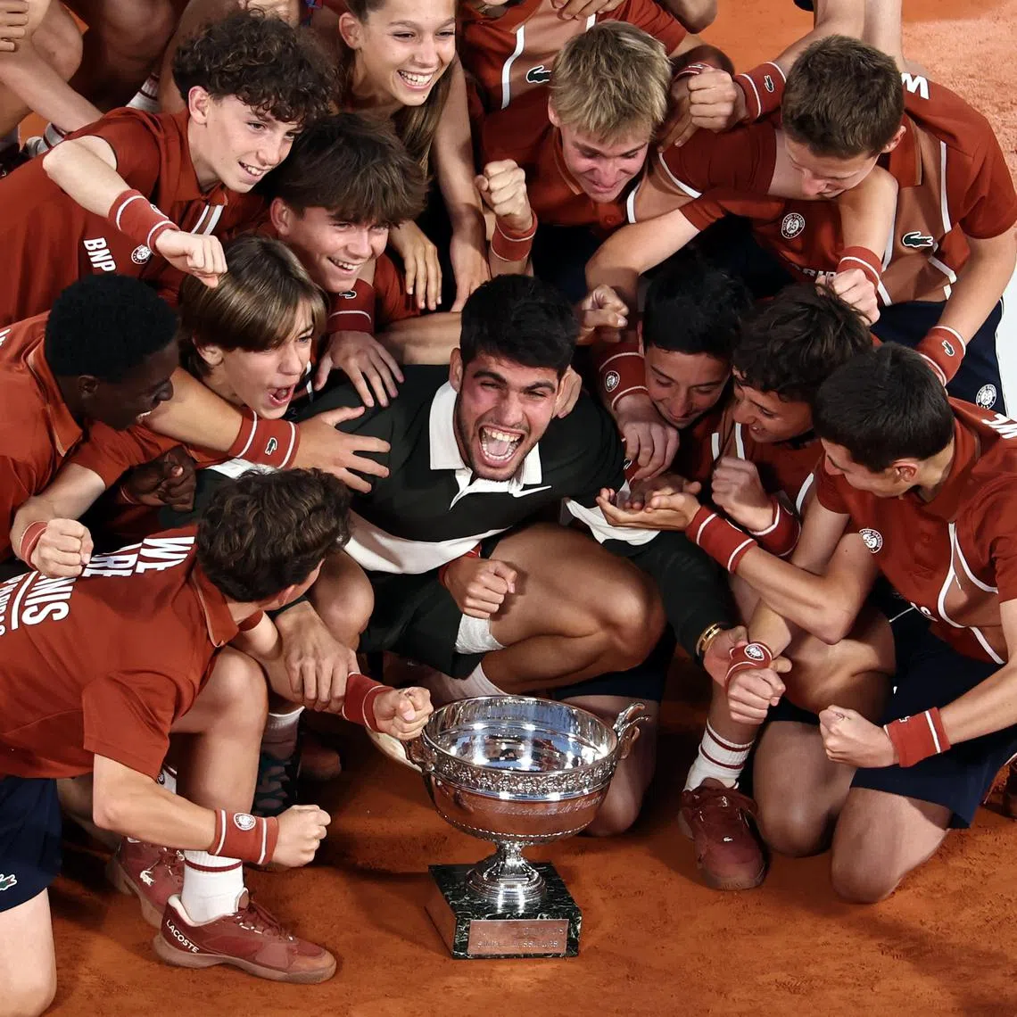 Carlos Alcaraz celebrates with the Coupe des Mousquetaires and ball kids after winning his match against Jannik Sinner at the French Open.