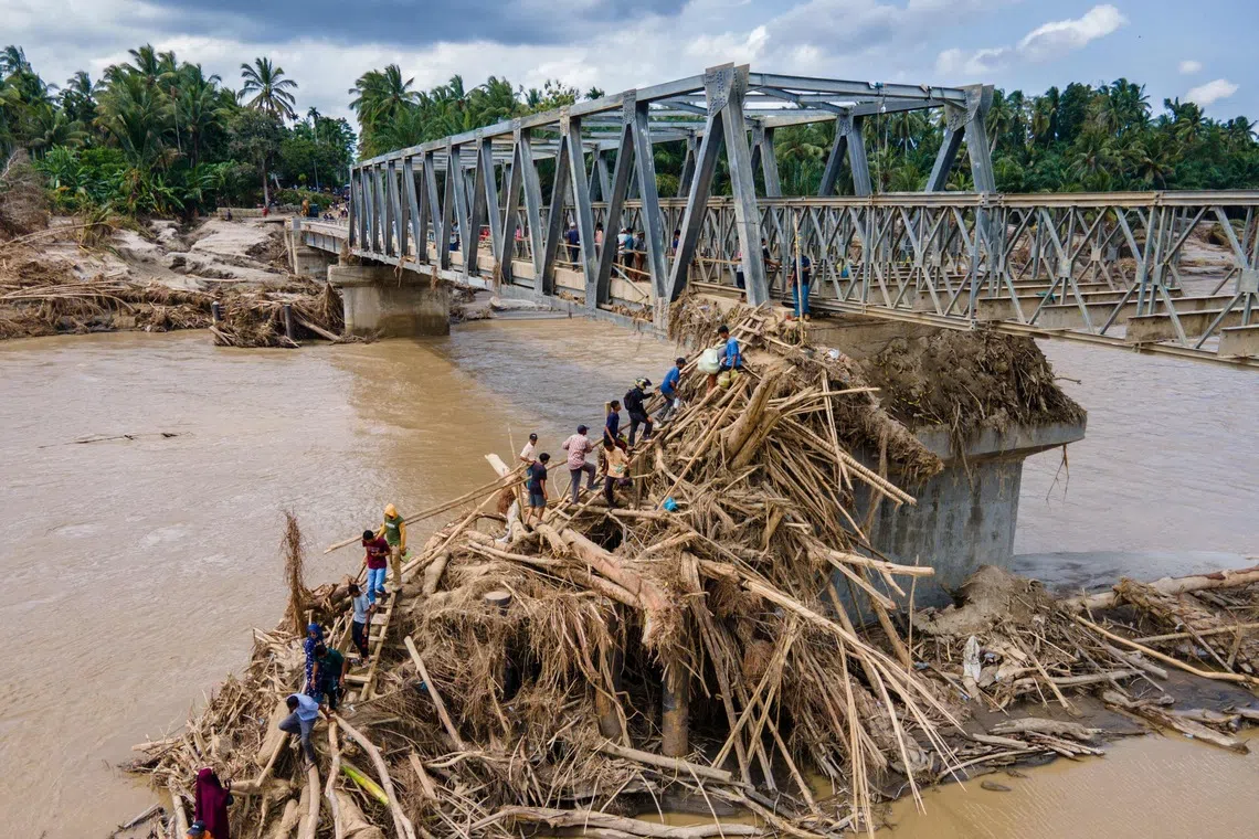 Residents climbing debris to cross the river on a newly built bridge connecting Aceh and North Sumatra province, after being destroyed by flash floods at Peusangan river in Bireuen district, Indonesia's Aceh province, on Dec 9, 2025. 