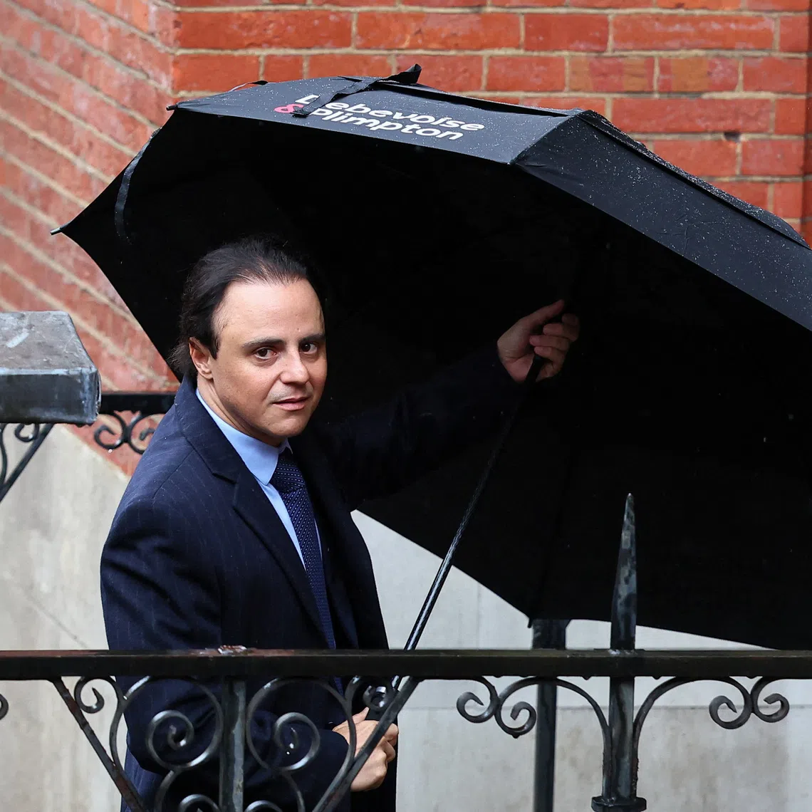 Former Ferrari Formula One driver Felipe Massa holds an umbrella near the High Court, where he is suing the governing FIA and former F1 chief Bernie Ecclestone, claiming he was the rightful 2008 world champion due to the Crashgate scandal at the Singapore Grand Prix and is seeking up to 64 million pounds in damages, in London, Britain, October 29, 2025. REUTERS/Isabel Infantes