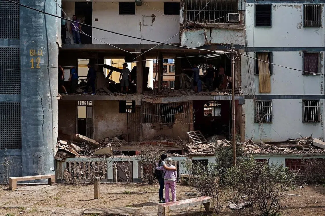 Women look at a damaged building as people inspect the rubble inside it, following U.S. strikes on Venezuela during which President Nicolas Maduro and his wife, Cilia Flores, were captured, in Catia La Mar, Venezuela, January 4, 2026. REUTERS/Gaby Oraa TPX IMAGES OF THE DAY