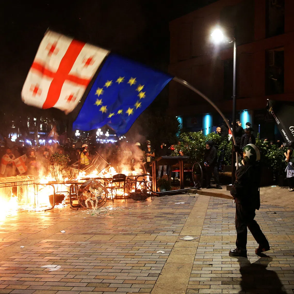 FILE PHOTO: A protester waves Georgian and EU flags in front of a burning barricade during an opposition rally on the day of local elections in Tbilisi, Georgia October 4, 2025. REUTERS/Irakli Gedenidze/File Photo