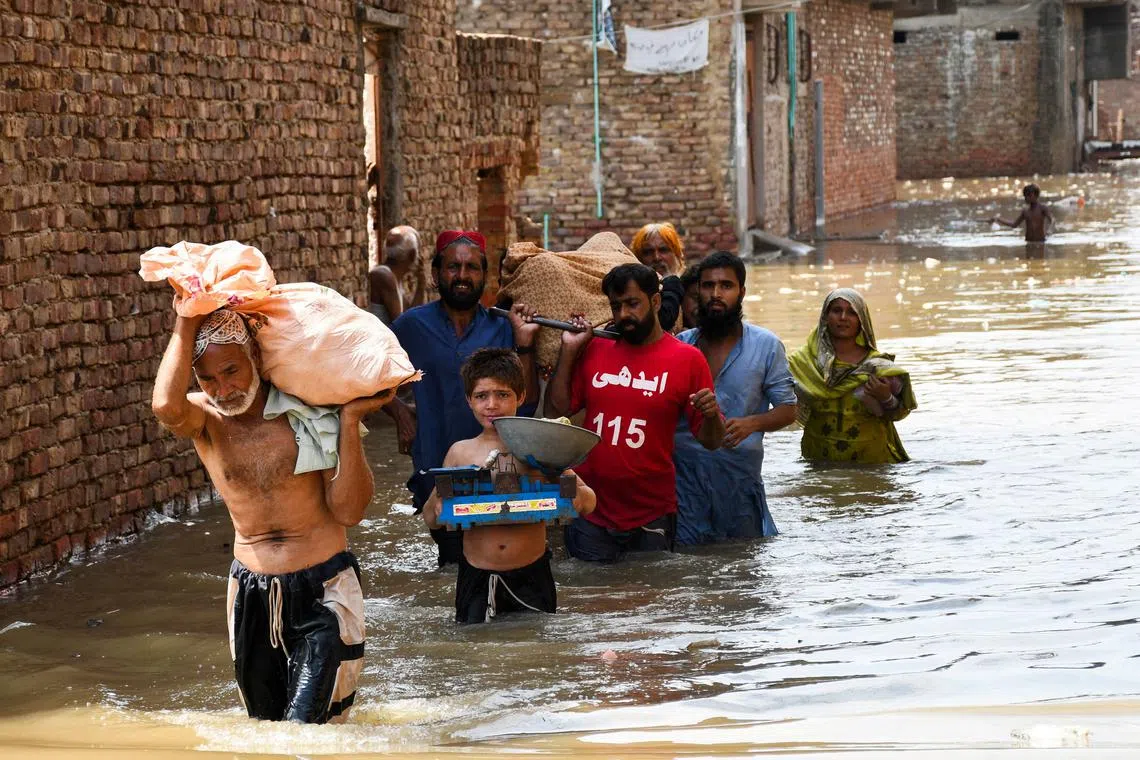 People wade through a flooded street as they carry a woman towards the hospital at Latifabad, Hyderabad, Pakistan, August 22, 2025. REUTERS/Yasir Rajput      TPX IMAGES OF THE DAY