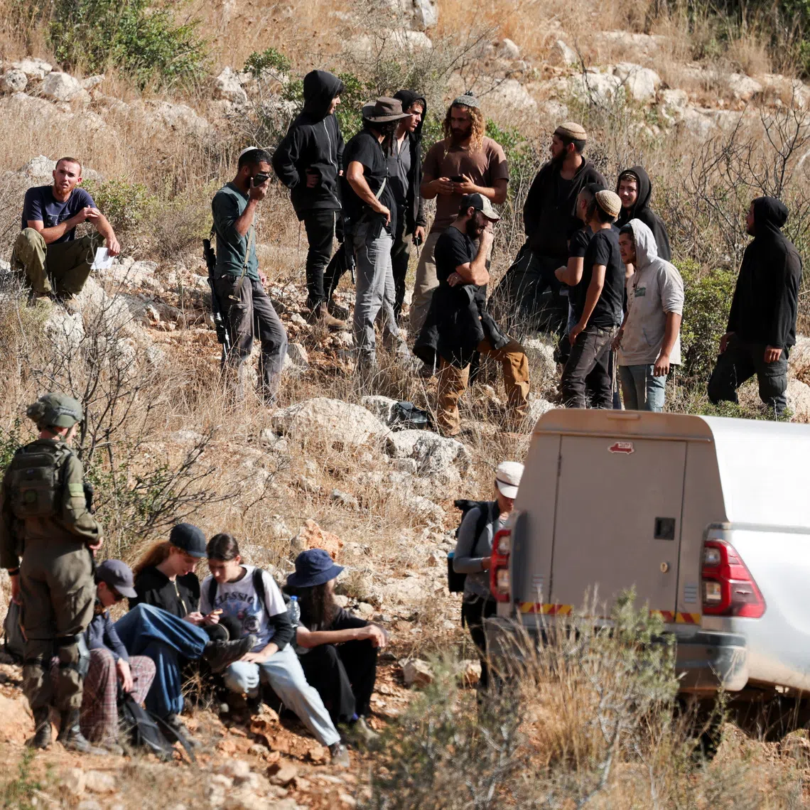Israeli activists sit next to members of the Israeli forces on guard, as they prepare to pick olives during the harvest season at Palestinian-owned olive groves in Deir Abu Mashal, near Ramallah, in the Israeli-occupied West Bank, October 19, 2026. REUTERS/Ammar Awad