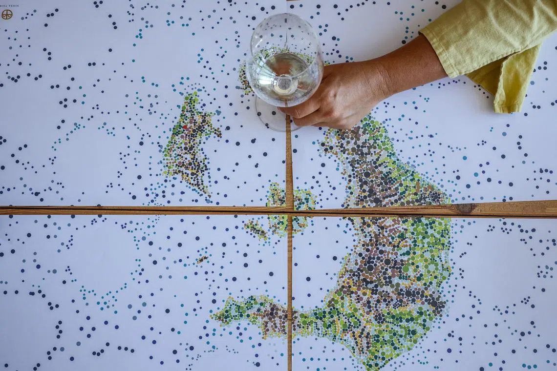 Ioanna Vamvakouri, president of the Santorini winemakers association holds a glass of awarded Assyrtiko wine at a placemat depicting the map of  Santorini island complex, in the winery at Therasia, Greece, June 24, 2026. REUTERS/Louisa Gouliamaki