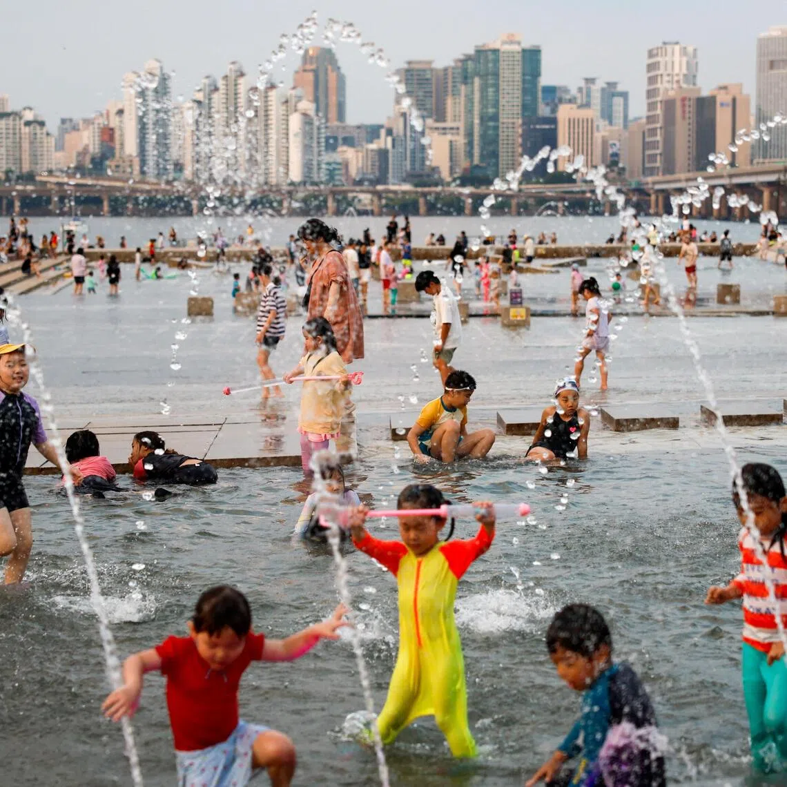 Children play in a fountain to cool off at a public water plaza along the Han River during a heatwave in Seoul, South Korea.