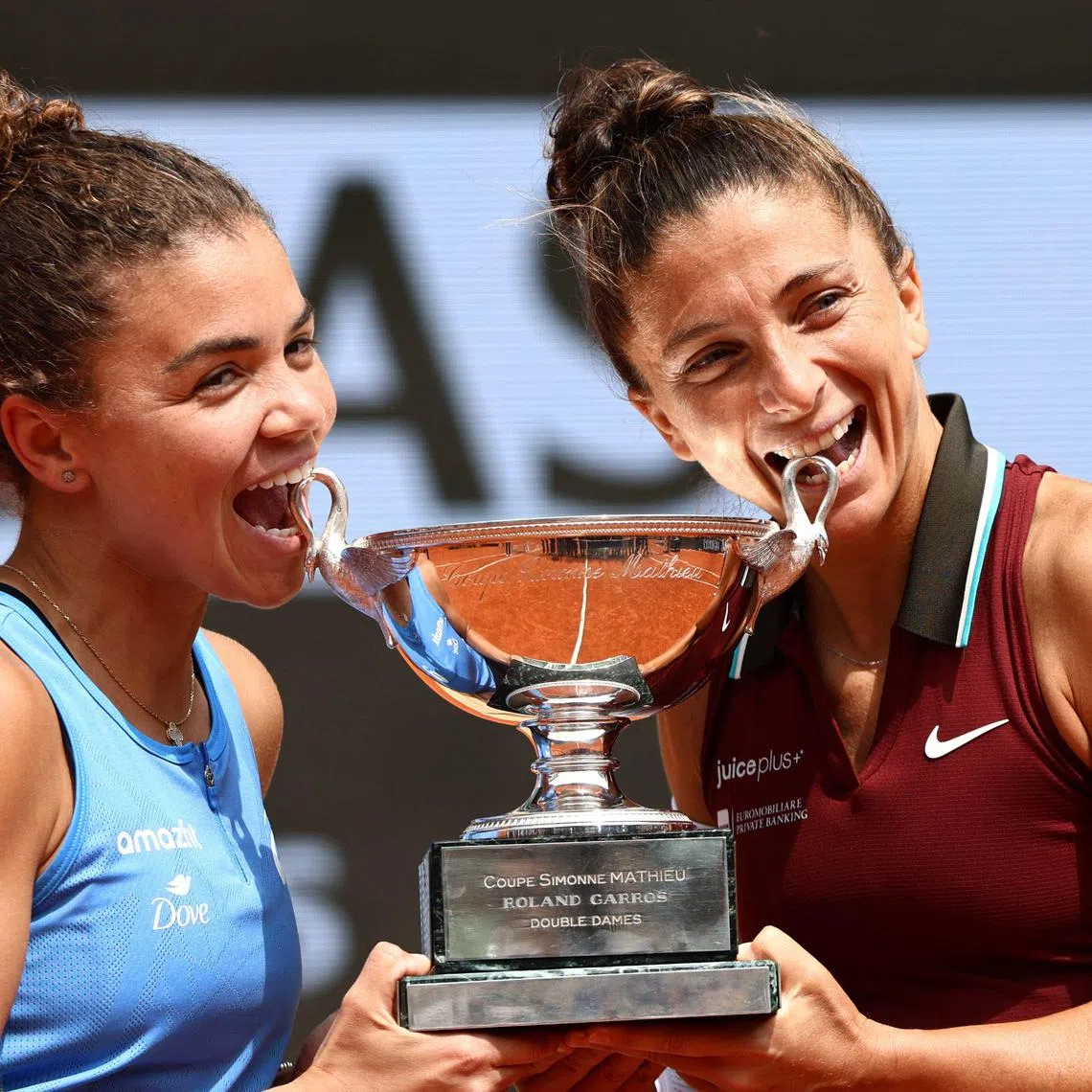 Italy's Jasmine Paolini (L) and Italy's Sara Errani bite their trophy as they pose after winning their women's doubles final match against Kazakhstan's Anna Danilina and Serbia's Alexandra Krunic on day 15 of the French Open tennis tournament on Court Philippe-Chatrier at the Roland-Garros Complex in Paris on June 8, 2025. (Photo by Thibaud MORITZ / AFP)
