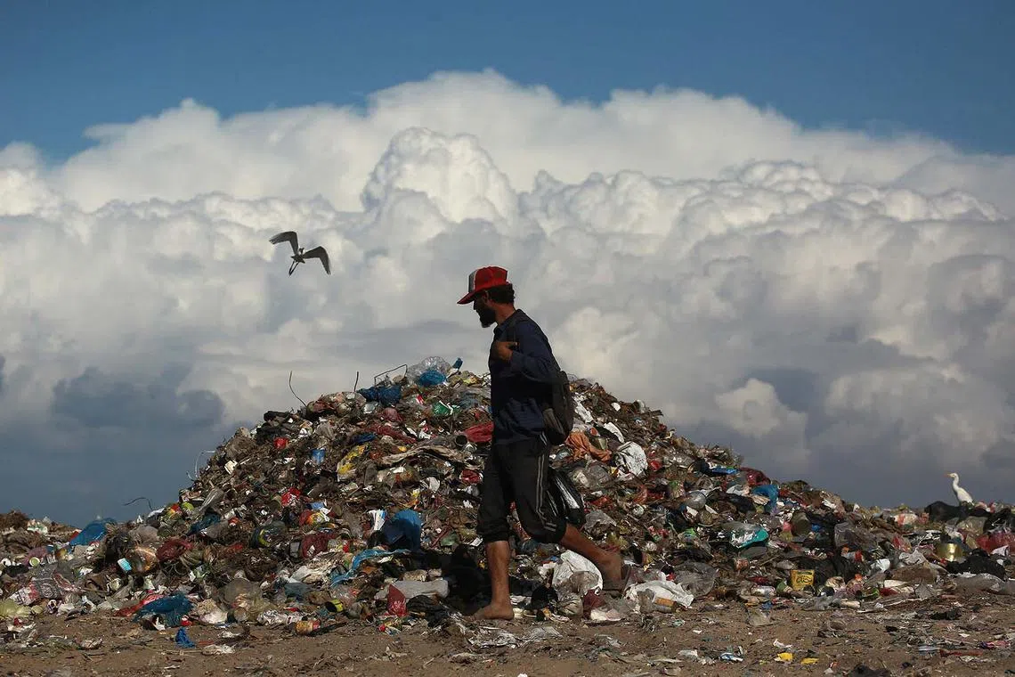 TOPSHOT - A man walks past a pile of garbage as he searches for things to rescue amid a humanitarian crisis the Gaza Strip, in Deir el Balah in central Gaza, on November 19, 2024, as the war in the Palestinian territory between Israel and Hamas continues. (Photo by Bashar TALEB / AFP)