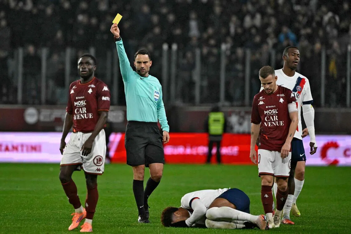 French referee Romain Lissorgue shows a yellow card to Metz's Ivorian defender Koffi Kouao after a foul on Paris Saint-Germain's French midfielder Desire Doue in the French Ligue 1 football match at the Stade Saint-Symphorien on Dec 13, 2025.