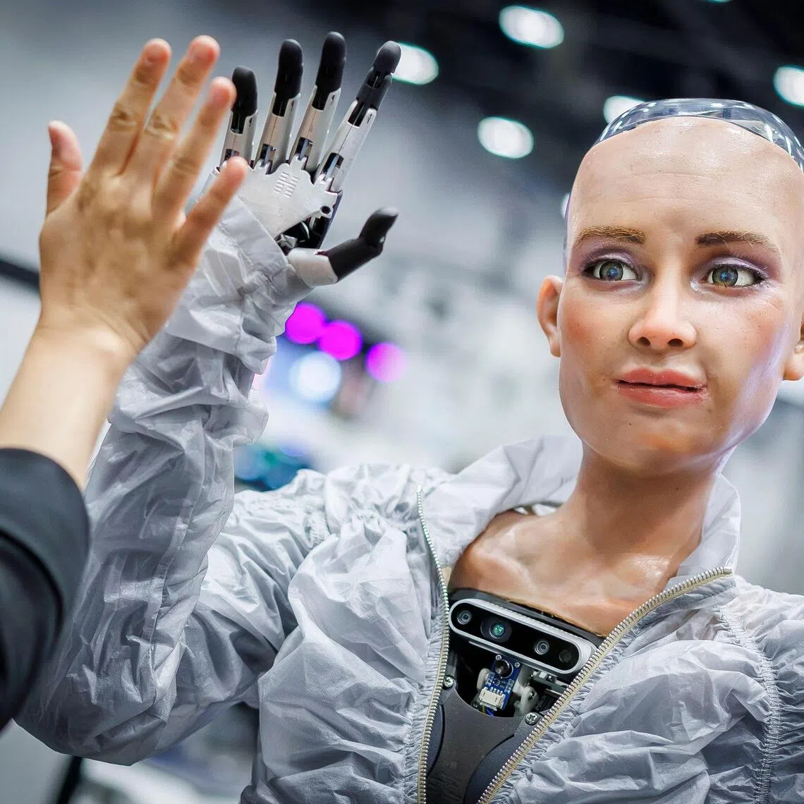 Sophie, a robot using artificial intelligence from Hanson Robotics, shares a high five with a visitor during the International Telecommunication Union (ITU) AI for Good Global Summit in Geneva on July 8, 2025. (Photo by Valentin Flauraud / AFP)