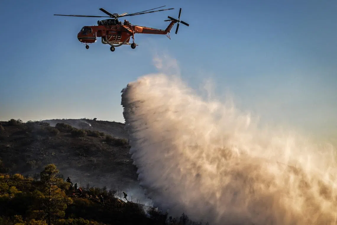 A firefighting helicopter releasing water on a forest fire, near Thymari, southeast of Athens, on June 26, 2025. 