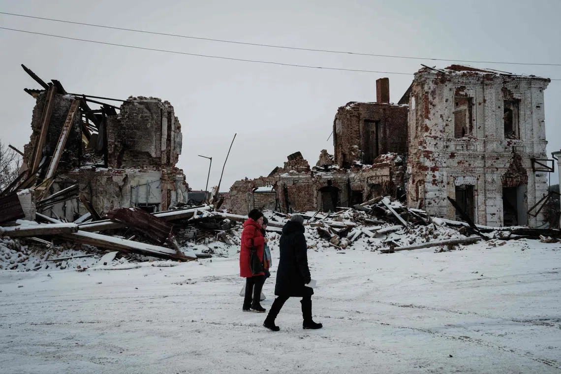 Pedestrians walk past a destroyed building in Kupyansk, in Ukraine's Kharkiv region, on Feb 13, 2023.