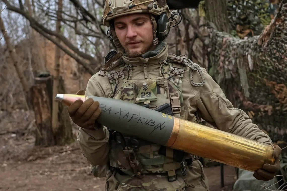 An Azov brigade serviceman prepares a howitzer shell for firing at Russian positions in Ukraine's Donetsk region, with an inscription saying "for Kharkiv".
