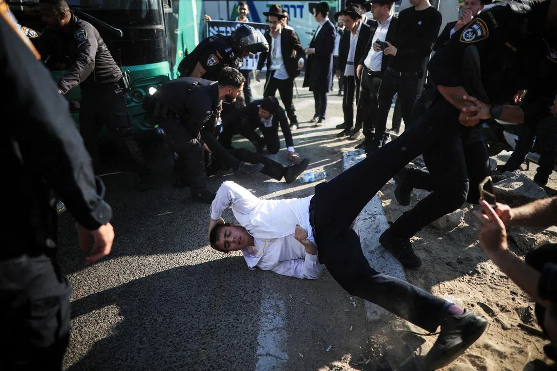 Israeli police taking away an Ultra-Orthodox Jew while people blocking a road take part in a protest against pressure to conscript into the military, in Bnei Brak, Israel, on June 5, 2025. 