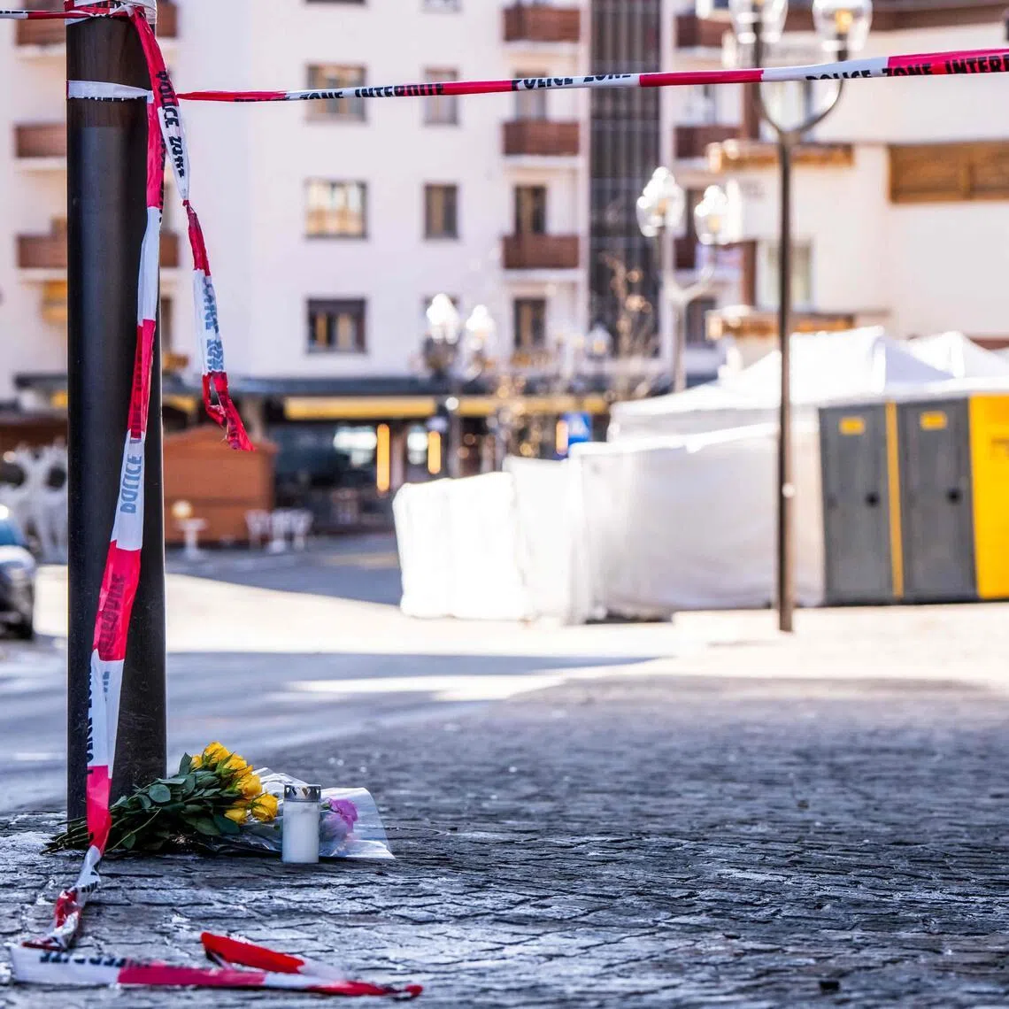 A photograph taken on January 1, 2026 shows flowers and candles laid on the ground near the bar Le Constellation following an explosion that ripped the venue in Crans-Montana, during New Year's Eve celebrations. Several dozen people are presumed dead and around 100 injured after a fire ripped through a crowded bar in the luxury Swiss ski resort town of Crans-Montana, police said early January 1, 2026. (Photo by MAXIME SCHMID / AFP)
