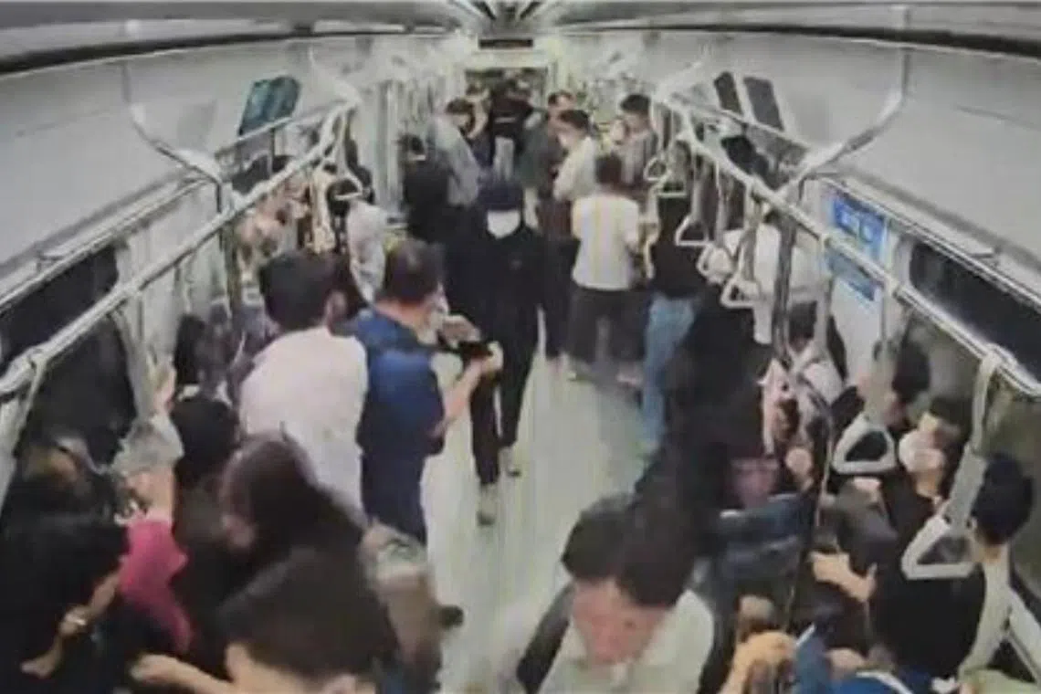 Footage shows the suspect in a black hoodie and mask (centre) forcefully pushing through passengers as he strides across the train aisle.