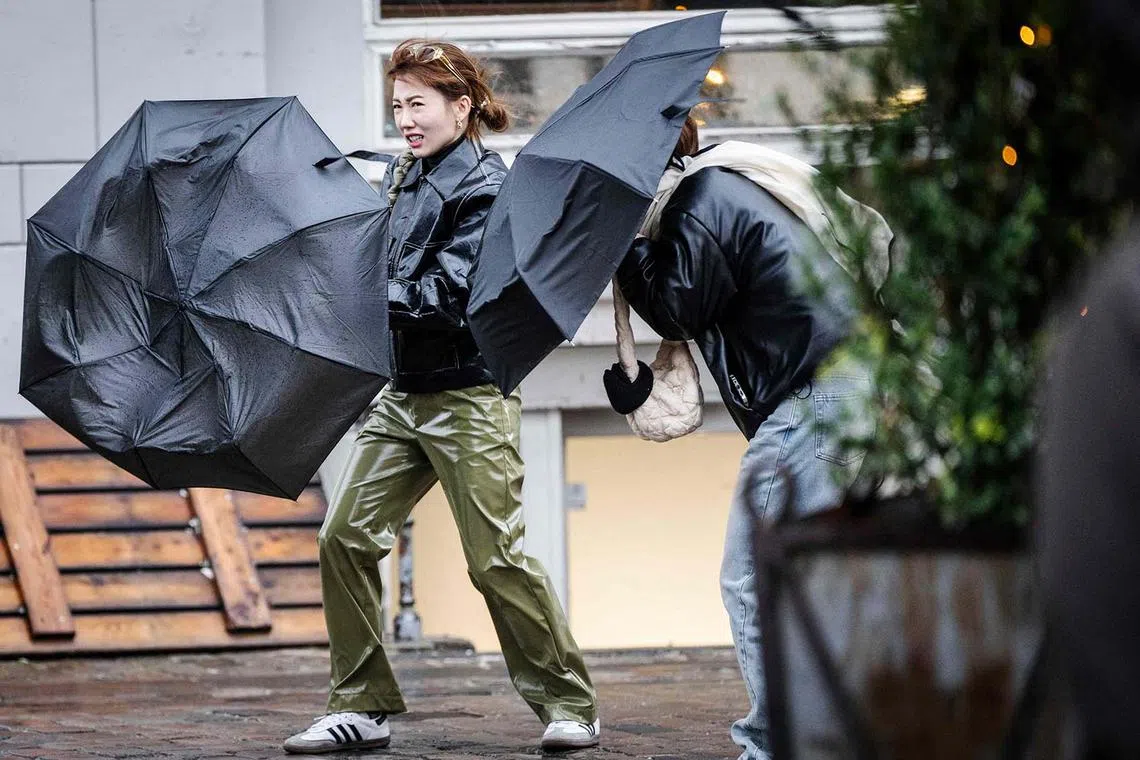TOPSHOT - Tourists struggle with the wind as they use umbrellas to protect against the rain in Nyhavn in Copenhagen, Denmark, on December 21, 2023. Danish meteorologists forecast dangerous weather conditions coming with storm Pia, including widespread flooding when the storm hits Denmark. (Photo by Thomas Traasdahl / Ritzau Scanpix / AFP) / Denmark OUT