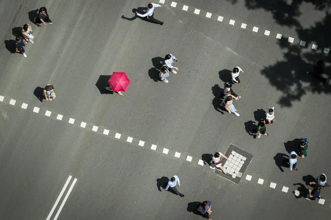 People crossing the road at Raffles Place, May 3, 2023. Singaporeans can expect April’s warm and humid weather to stretch into the next two weeks. Daily temperatures could reach up to 34 deg C on most afternoons in the first half of May, normally the warmest month of the year.