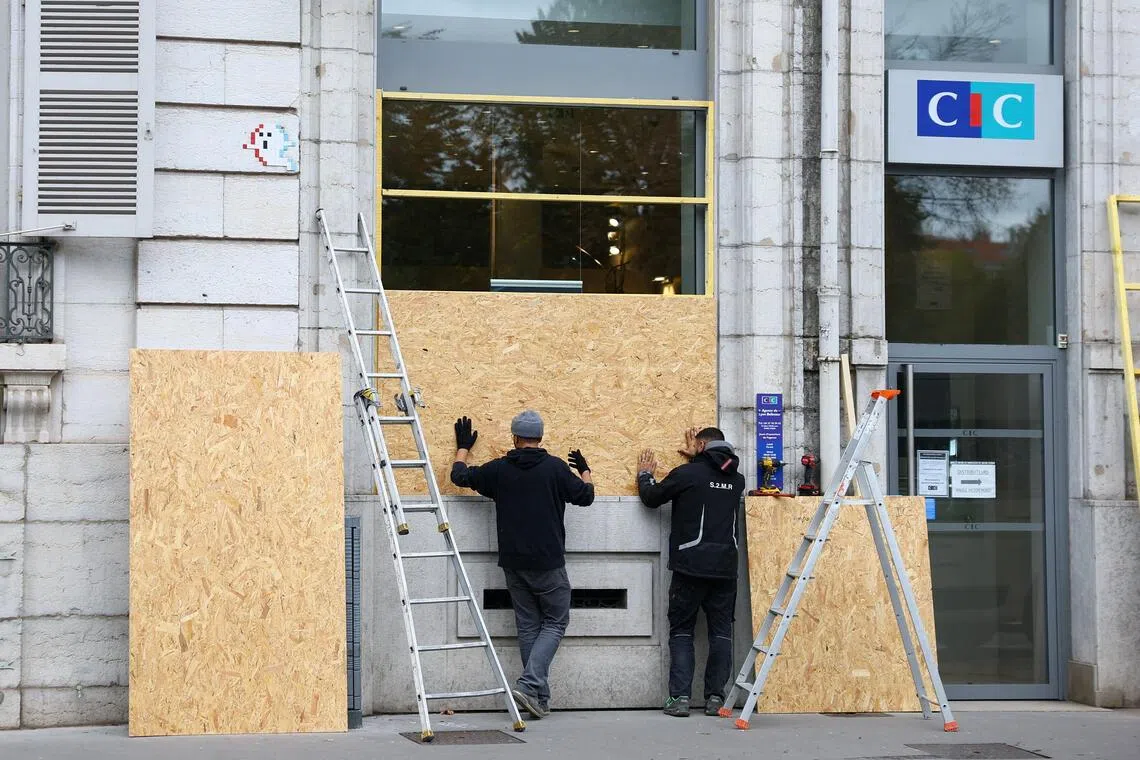 Workers install wooden panels to protect the storefront windows of a CIC bank branch in Lyon ahead of nationwide protests on Oct 24.