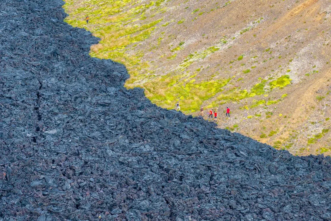 People walking past dried lava (left) from a previous volcanic eruption as they make their way to a location closer to watch the fresh volcano eruption near Grindavik, Reykjanes, Iceland, on July 17, 2025. 