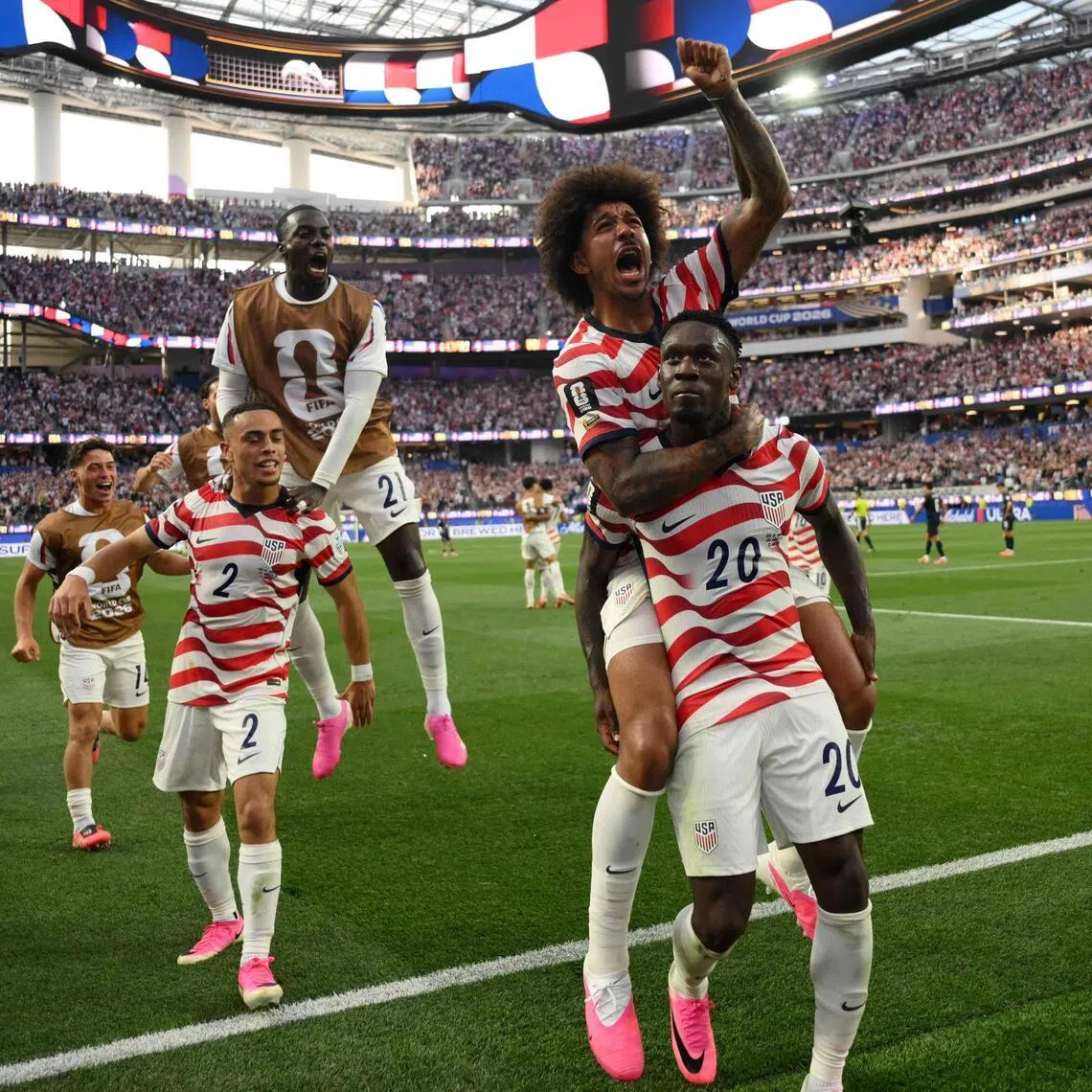 US forward Folarin Balogun (No. 20) celebrates with teammates after scoring his team's third goal during the 2026 World Cup Group D football match between US and Paraguay at the Los Angeles Stadium.