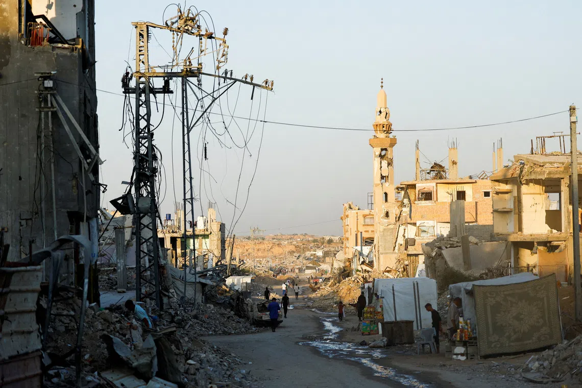 People walk past damaged electricity poles in Nuseirat, central Gaza Strip, October 31, 2025. REUTERS/Mahmoud Issa