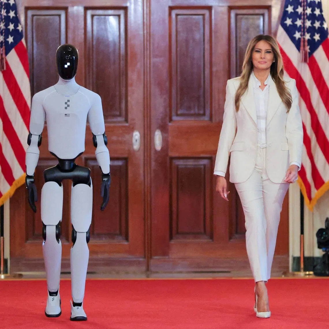 U.S. first lady Melania Trump walks next to a humanoid robot as she hosts a roundtable event on the second day of the inaugural Fostering the Future Together Global Coalition Summit, at the White House in Washington, D.C., U.S., March 25, 2026. REUTERS/Kylie Cooper