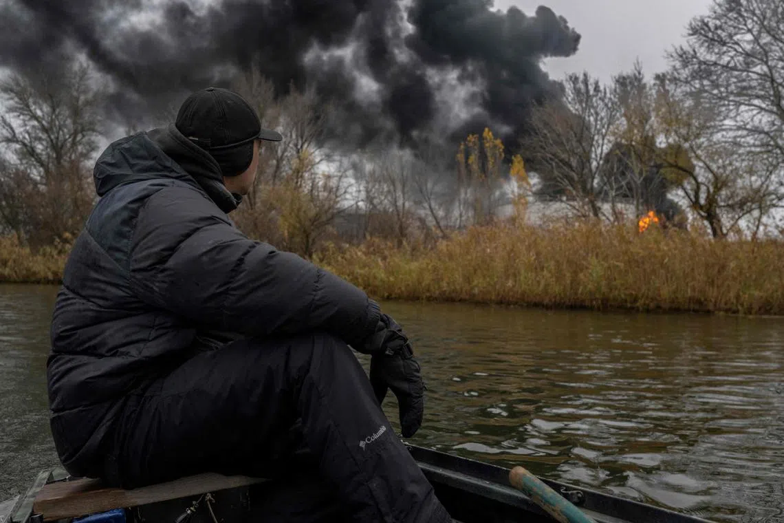 A fisherman sailing past burning oil reserves along the Dnipro River in Kherson, Ukraine, on Nov 20, 2022.