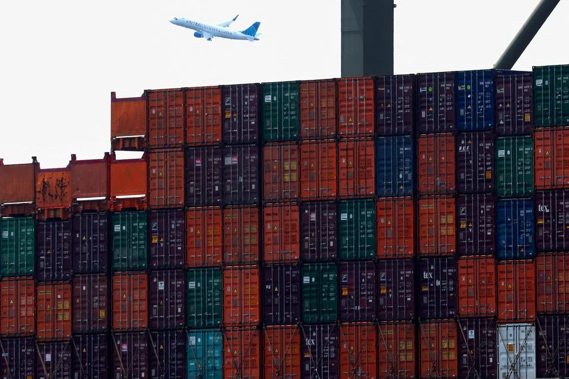 FILE PHOTO: Shipping containers are seen stacked on a docked cargo ship as a passenger airplane takes off from Newark Airport, in Port Elizabeth, New Jersey, U.S., July 12, 2023. REUTERS/Mike Segar/File Photo