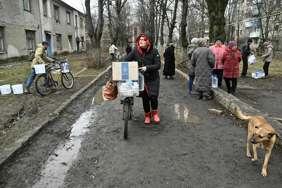 Local residents carry home humanitarian aid - water containers and food boxes - in the town of Chasiv Yar, in Ukraine's Donetsk region.