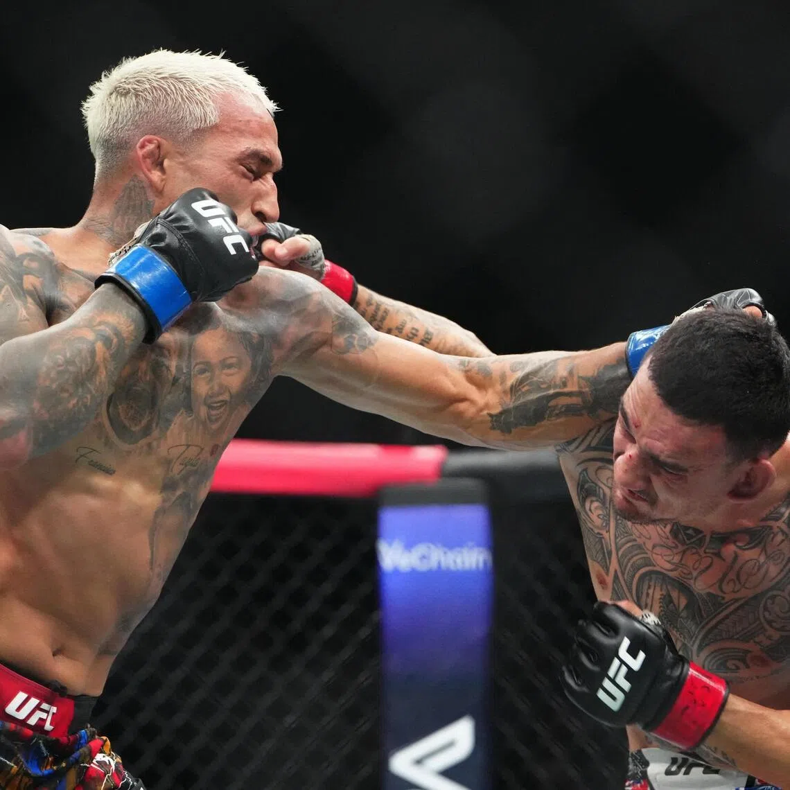 Max Holloway (red gloves) fights Charles Oliveira (blue gloves) during UFC 326 at T-Mobile Arena. 