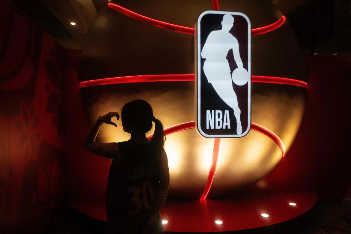 A fan posing next to the National Basketball Association logo before the NBA pre-season basketball game between the Phoenix Suns and Brooklyn Nets at the Venetian Arena in Macau on Oct 12, 2025.