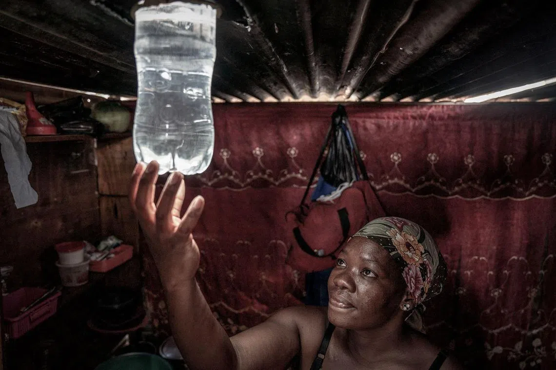 A resident looks at the light beaming from a freshly installed Amandla Elanga bottle globe inside her shack in an informal settlement in Olievenhoutbosch, Centurion. The bottle globe provides day light from a two litre plastic bottle installed onto the roof of a shack by reflecting light from the sun: it contains a solution of water and and household bleach which also disinfects the water. 