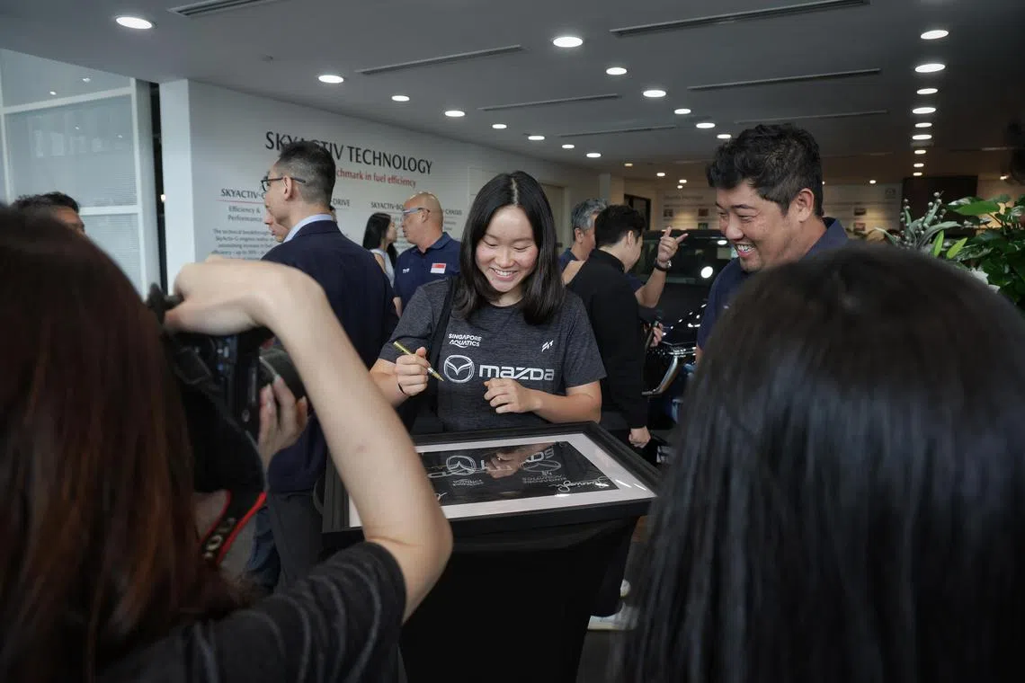 National swimmer Gan Ching Hwee signing an autograph on a framed t-shirt commemorating the sponsorship signing ceremony between Singapore Aquatics and Mazda Singapore on July 10, 2024. On the right is national swimming head coach Gary Tan. ST PHOTO: KEVIN LIM dgswim10
