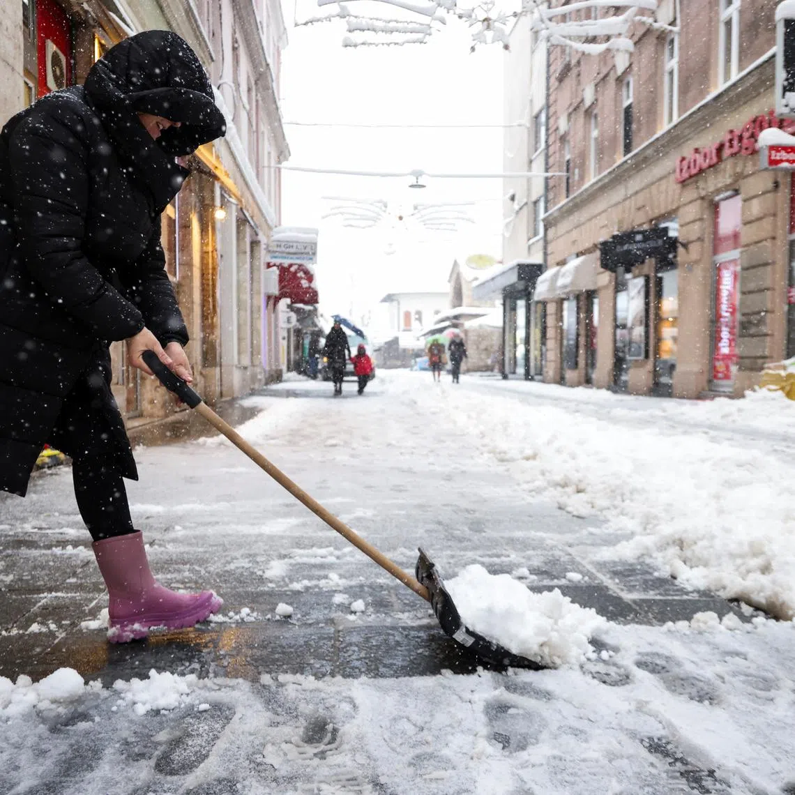 A woman shovels snow on the main street during snowstorm in Sarajevo, Bosnia and Herzegovina, December 24, 2024.REUTERS/Amel Emric