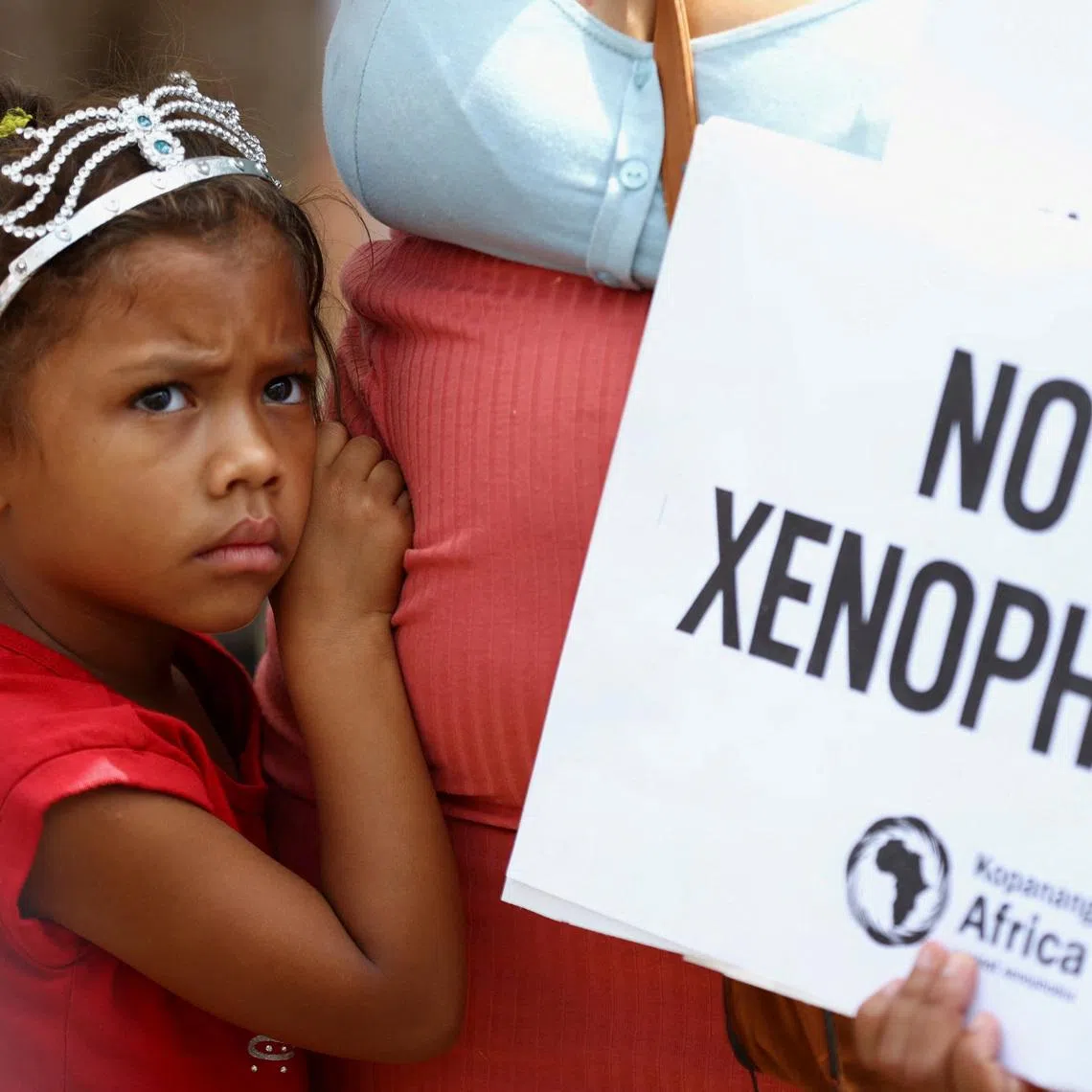 FILE PHOTO: A child looks on next to her mother holding a placard, during a march by a South African anti-xenophobia group following a recent campaign by another group which called on the government to prioritise jobs for nationals and remove undocumented immigrants from the country, in Hillbrow, Johannesburg, South Africa, March 26, 2022. REUTERS/ Siphiwe Sibeko/File Photo