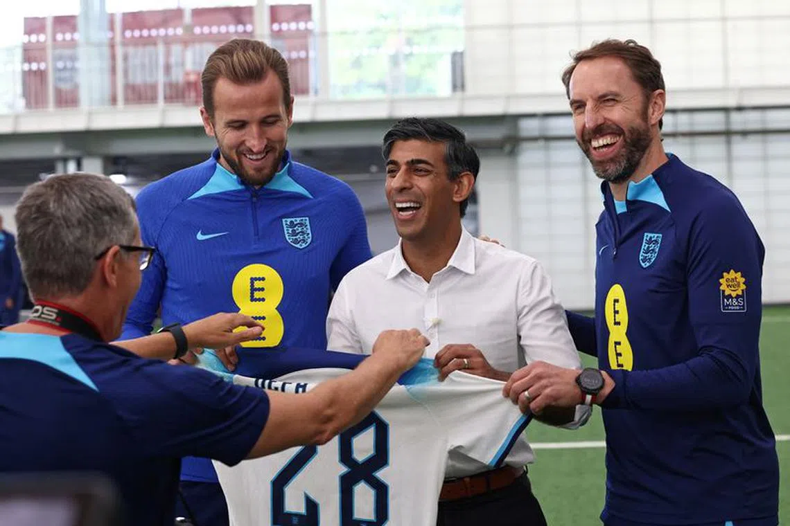 A photographer directs Britain's Prime Minister Rishi Sunak in how to pose with an England football shirt, as he stands alongside England's striker Harry Kane, and England's manager Gareth Southgate during a visit to England's football training centre at St George's Park in Burton-on-Trent, Britain, October 10, 2023. Seven years after awarding Euro-2024 to Germany, UEFA announced on October 10, 2023 the hosts for the next two editions: The United Kingdom and Ireland are due to host the tournament together in 2028, followed by the unprecedented tandem of Italy and Turkey in 2032.     DARREN STAPLES/Pool via REUTERS