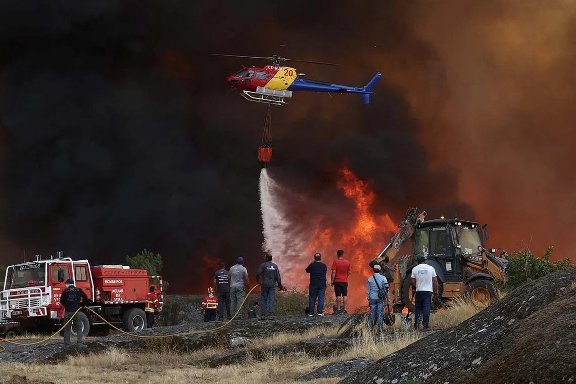 A helicopter droppings water on a wildfire approaching Trancoso, Portugal, Aug 13, 2025. 