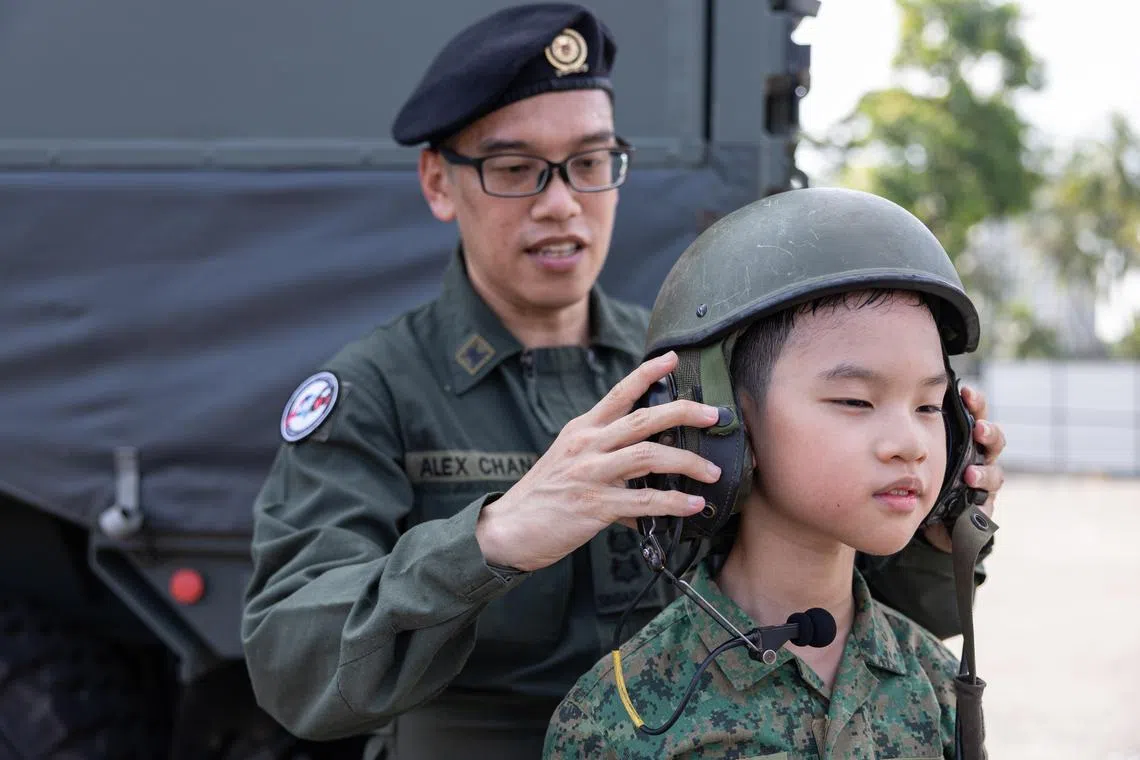 ST20250621_202565800959/azcolumn21/Brian Teo/Ahmad Zhaki Bin Abdullah/*EMBARGO UNTIL JUNE 23, 6AM*  Lieutenant Colonel (NS) Alex Chan Kwok Hoh (left), 48, Mobile Column Commander, helping his son Chan Jinghoi, 10, put on his helmet at the F1 Village during the NDP Media Event 3 on June 21, 2025. ST PHOTO: BRIAN TEO