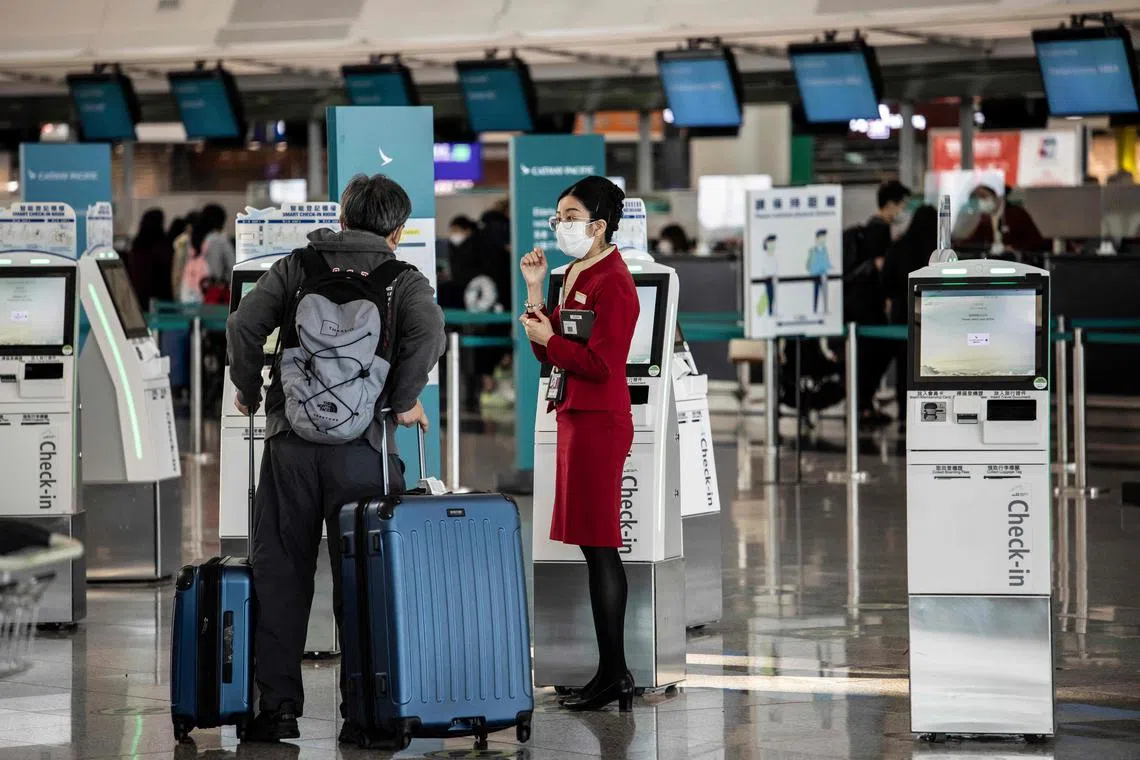 A ground staff member helping a passenger next to a self check-in kiosk at Hong Kong International Airport.
