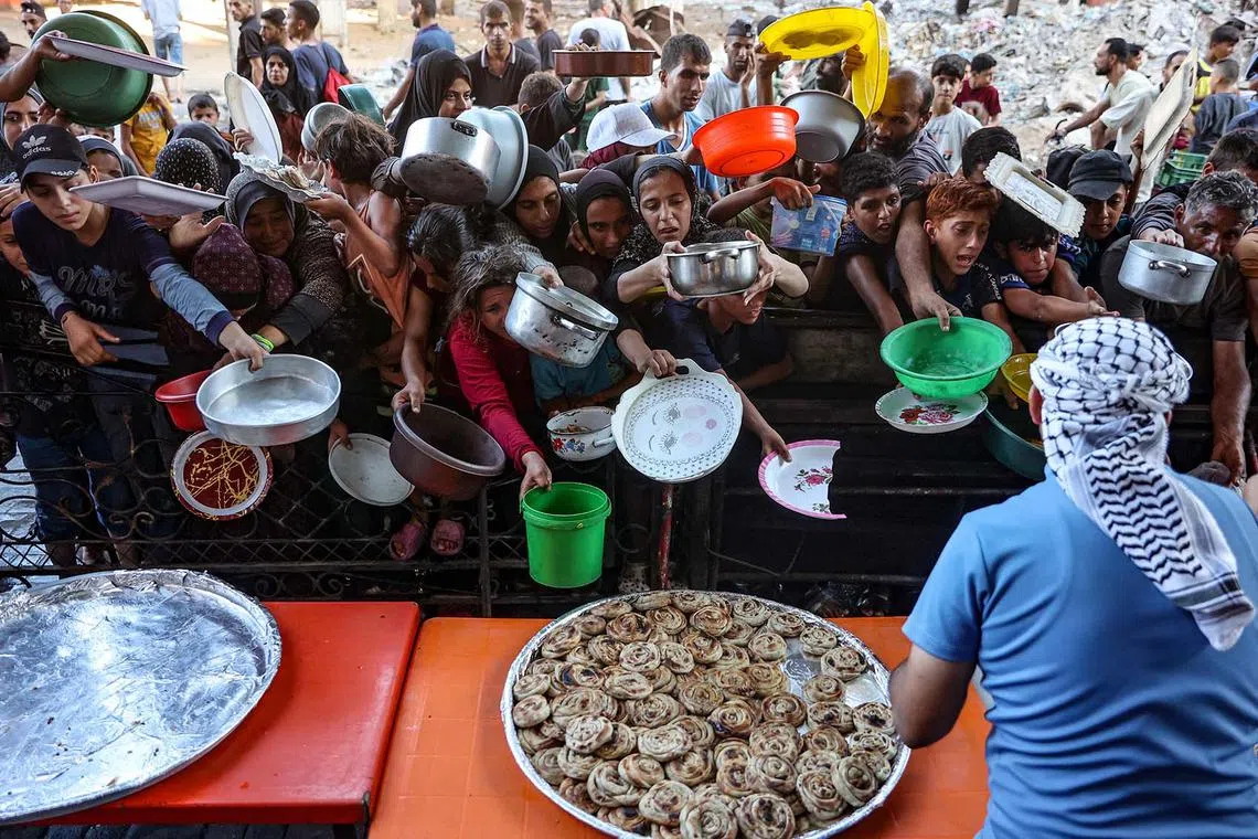Palestinians, mostly children, holding out their plates toward a man, to receive their share of vegetable patties prepared by volunteers in Beit Lahia in the northern Gaza Strip on Aug 14, 2024.