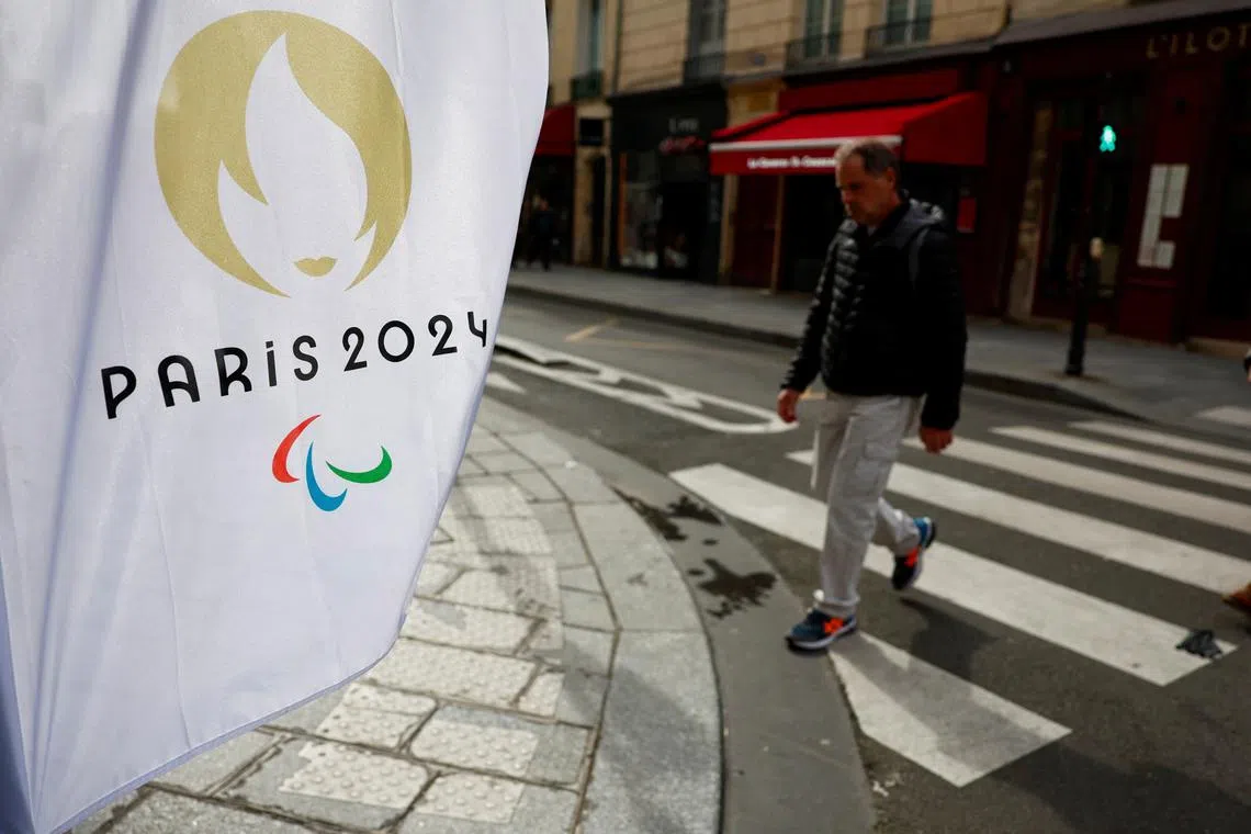 A man walks near a flag with the logo of the Paris 2024 Olympic and Paralympic Games in Paris, France, March 25, 2024. REUTERS/Gonzalo Fuentes/File Photo