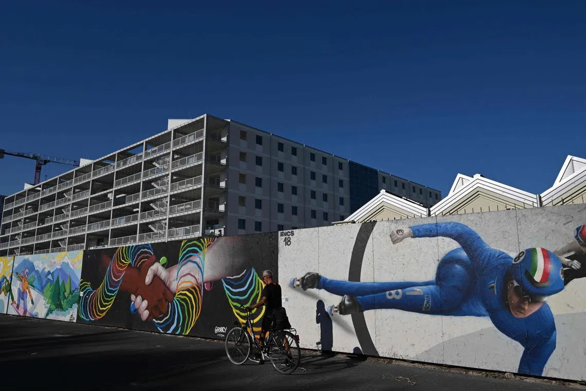 A local resident cycling past the Milano-Cortina 2026 Olympic Village construction site, in Milan on July 31, 2025. The Winter Olympic Games Milano-Cortina 2026 will take place from Feb 6 to 22 and the Winter Paralympic Games from March 6 to 22, 2026. 