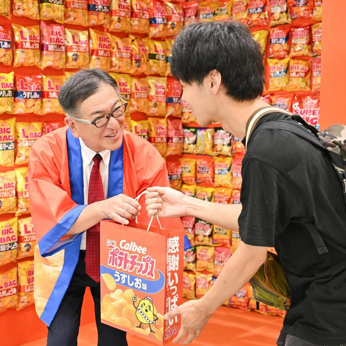 A passer-by receives a bag of Calbee potato chips from Calbee Group chief executive officer Makoto Ehara, at an event held at Tokyo Station on Sept 1 to commemorate the brand's 50th anniversary of potato chips.