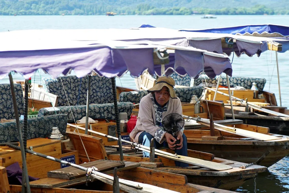 A boatman holds a portable fan as he waits for customers in a boat on the West Lake, amid a red alert for heatwave in Hangzhou, Zhejiang province, China August 2, 2024. REUTERS/Nicoco Chan