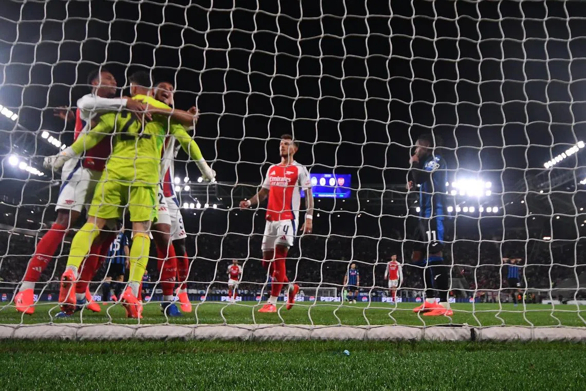 Arsenal's David Raya celebrating with teammates after saving a penalty during the Champions League match against Atalanta and at the Bergamo Stadium.