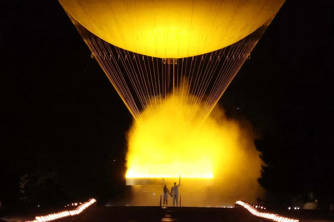 TOPSHOT - The torchbearers French former sprinter Marie-Jose Perec and French judoka Teddy Riner stand next to a lit Olympic cauldron during the opening ceremony of the Paris 2024 Olympic Games in Paris on July 26, 2024. (Photo by David GRAY / AFP)