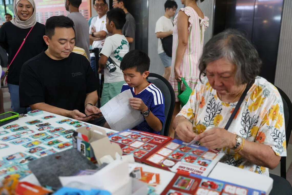 Retiree Dolly Goh (right), 78, helping her 10-year-old grandson Gyan Phua paste stickers into his album.