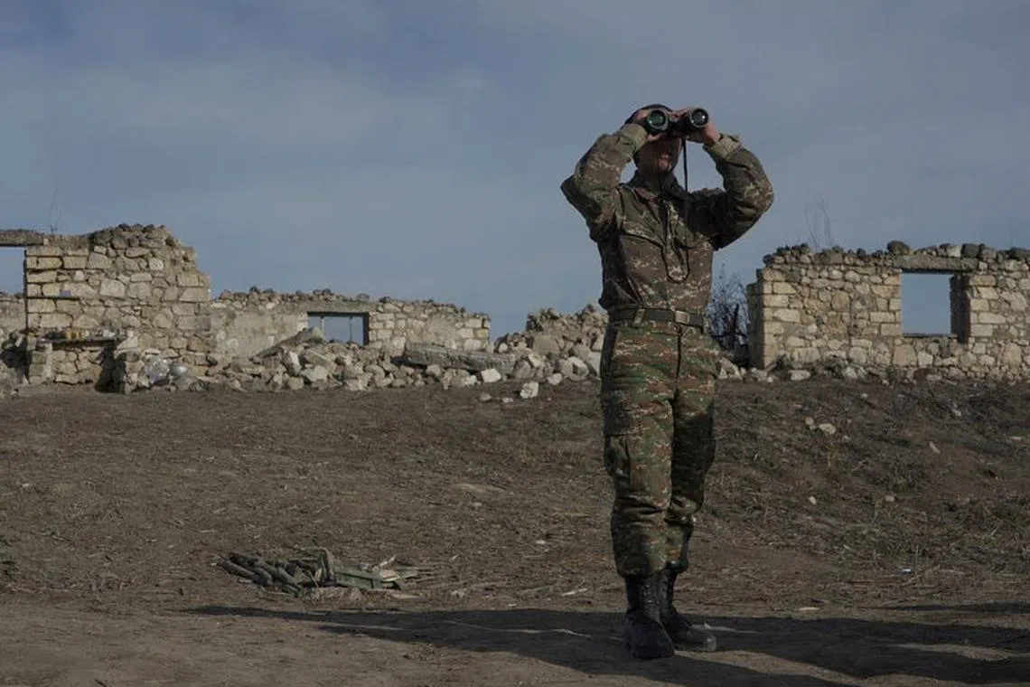 FILE PHOTO: An ethnic Armenian soldier looks through binoculars as he stands at fighting positions near the village of Taghavard in the region of Nagorno-Karabakh, January 11, 2021. REUTERS/Artem Mikryukov/File Photo
