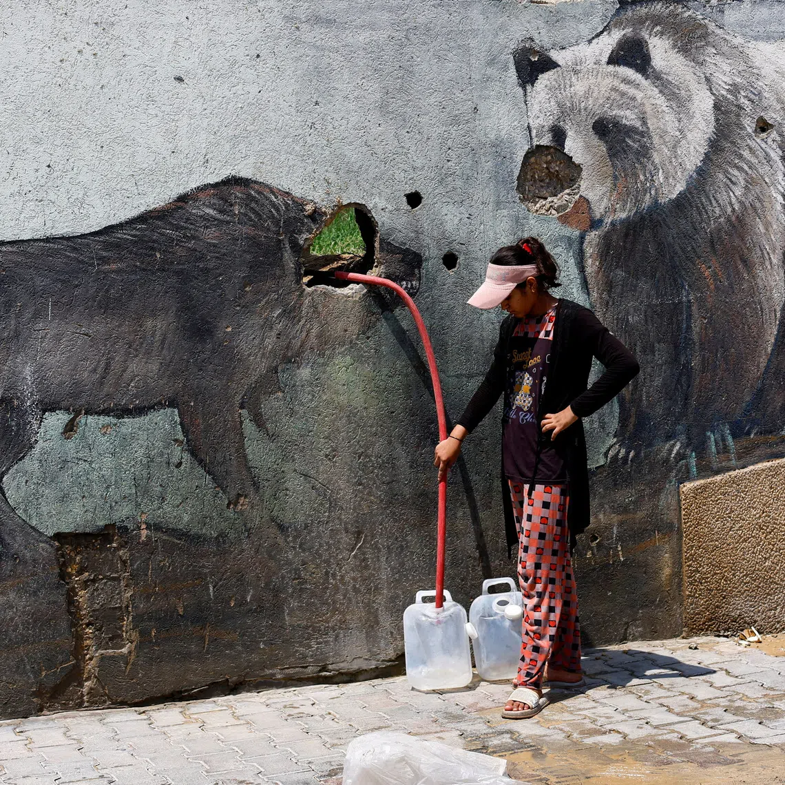 A Palestinian girl fills water containers outside the wall of a zoo damaged during the war, in Gaza City, August 15, 2026. REUTERS/Mahmoud Issa     TPX IMAGES OF THE DAY